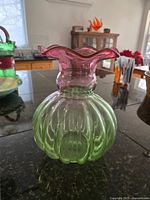 Front view showing the melon-shaped green glass body and ruffled cranberry pink top rim