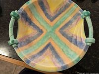 Top-down photograph of the Art Deco console bowl showing its chevron multicolor pattern and green tubular handles.