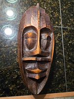 Front view of the wooden carved tribal mask showing geometric facial features and dark brown color.