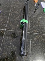 Retractable baby gate rolled up and secured with a green clip, showing end of the housing and black mesh fabric on tiled floor.