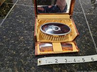 Open hinged grooming box showing oval child's brush with faux tortoise shell back and two small matching combs inside satin-lined interior with mirror lid