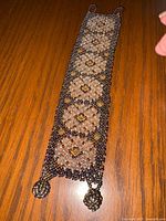 Full view of handmade beaded bracelet laid flat showing floral and geometric bead pattern and bead spheres at ends.