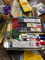 Photo of assorted paint brushes, pencil sharpener, crayons, pencils, markers, and markers in a metal container