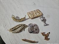 Six brooches and one hair clip laid out on a white surface with visible wear and patina.