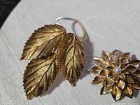 Photo of front side showing gold-tone leaf scarf clip and flower brooch with faux pearl center.