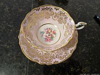 Top view of pink tea cup placed inside matching saucer, showing floral bouquet center and gold ornamental designs