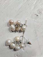 Top view, close up of two real pearl cluster earrings, showing five pearls per earring with silver-tone metal hooks.