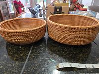 Two round woven baskets side by side from the front showing weave details and size comparison with measuring tape in front.