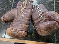 Pair of brown leather boxing gloves with laces, showing wear and creasing in the leather, displayed together.