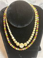 Two necklaces displayed on black velvet stand; one is pink and green glass cats eye beads, the other mother of pearl beads including larger central beads