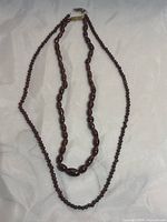 Photo of two garnet beaded necklaces displayed on light fabric, showing both necklaces fully.
