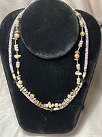Full view of two necklaces on a black velvet bust. Both necklaces combine small heishi shell beads, pearls, and amethyst stones, showcasing purple and natural beige tones.