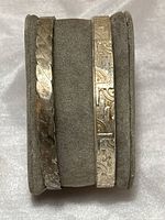 Two silver bangle bracelets displayed side by side on a gray stand showing their different designs.