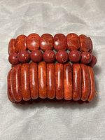 Three red coral stretch bracelets stacked together on a light-colored fabric background.