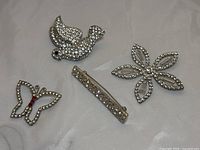 Four rhinestone brooches displayed on a flat surface including butterfly, dove, flower, and bar designs.