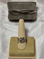 Front shot of the silver hinged bangle bracelet and diamond ring on separate stands, showing intertwined diamond design on bracelet and criss-cross diamond ring.