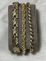 Set of three bracelets displayed on grey velvet jewerly holder showing the designs and two-tone coloring.