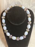 Necklace displayed on a black velvet bust showing the arrangement of light blue agate beads, purple amethyst clusters, and green peridot chips with a metal clasp.