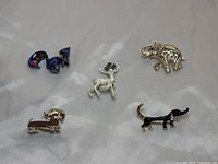 Five animal enamel and metal brooches displayed on a light grey background, showing all five pins including a purple squirrel, gold elephant, Christmas deer, and two dachshund pups.