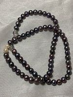 Black pearl necklace laid out on a cloth background, showing round pearls and a single clear crystal accent bead.