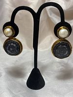 Front view of both clip on earrings displayed on black velvet stand showing white pearl tops and black geometric quartz stones set in brass bezels.