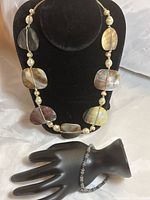 Front view of conch shell necklace on stand and silver & hematite bead bracelet on black hand display
