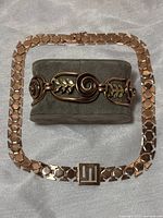 Copper bracelet and necklace displayed separately on a grey cloth.