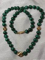 Photo of the malachite bead necklace with gold filled clasp and decorative beads laid out on a white cloth.