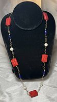 Full view of the necklace on a black stand showing the arrangement of carved red resin beads, white pearls, and blue lapis lazuli beads linked with gold filled chain.