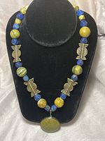 Full view of the necklace showing green jasper, lapis lazuli, and brass beads strung together, displayed on a black bust stand.