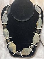 Full view of the necklace on black display showing large labradorite stones, white pearls, and black speckled stones.