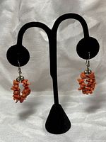Front view of the pair of red coral earrings displayed on a black earring holder. Shows the cluster of multiple red coral chip beads and silver beads near the hook.