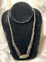 Full view of necklace displayed on black velvet stand showing wood heishi beads and turquoise nuggets at center.