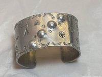 Front angle view of the aluminum cuff bracelet showing raised dome details and stamped Native American motifs including stars, crescents, and animals.