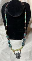 Full view of the necklace displayed on a black bust showing the bead arrangement including turquoise chips, larger blue beads, red coral and black beads with the wolf pendant.
