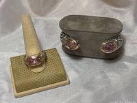 Photo showing ring displayed on a beige ring stand and the silver-tone hinged cuff bracelet on a grayish display pillow. Both items feature pink faceted crystals and two-tone metal design.