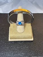 Photo showing polished stainless steel cuff bracelet with 'debra' inscription on gold-tone plate and blue and white crystal ring on display stand.