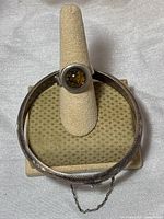 Photo showing the amber ring mounted on a ring stand and the matching sterling silver bangle with flower pattern and safety chain on a cushioned display.