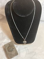 Full display of the heart-shaped silver locket pendant on beaded necklace, with Missouri Valley Conference medal placed beside it on a white surface.