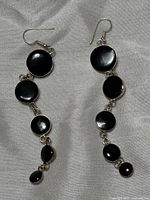 Pair of earrings laid flat showing five linked black enamel discs descending in size with sterling silver settings and hooks
