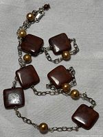 Necklace laid flat showing the red agate square stones and golden orange pearls connected with sterling silver chain links.
