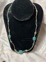 Front view of the full turquoise necklace on a black display bust showing turquoise stones, silver tubular links and beads.