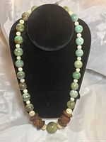 Full view of the turquoise necklace showing beads of turquoise and carved wooden and ivory-colored beads on a black jewelry display.