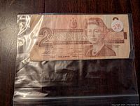 Single Canadian two dollar bill in a protective plastic sleeve, showing front side with Queen Elizabeth II portrait, denomination, and year 1986.