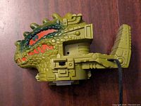 Front angled view of the green plastic Dragon Walker vehicle showing the detailed dinosaur head shape with painted red teeth accents and mechanical detailing.