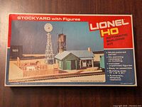 Box lid showing the Lionel HO Stockyard Building model kit image and text, highlighting features such as multicolored parts, no painting required, unpainted figures included, easy assembly, and size.