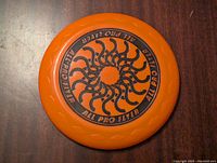 Top side of orange plastic frisbee showing black sun-like pattern and 'ALL PRO FLYER' text