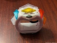Photo showing front view of white Pokemon Z-Ring with yellow, red, orange and blue gem-like shapes on edges
