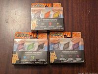 Front view of three unopened packages of Pokémon Z-Crystals each containing three crystals of different types/elemental attributes.