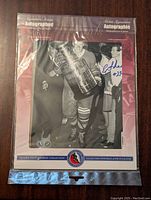 Front view of black and white signed photo of Eddie Shack holding the Stanley Cup with blue ink signature and #23. Framed with Frameworth branding.